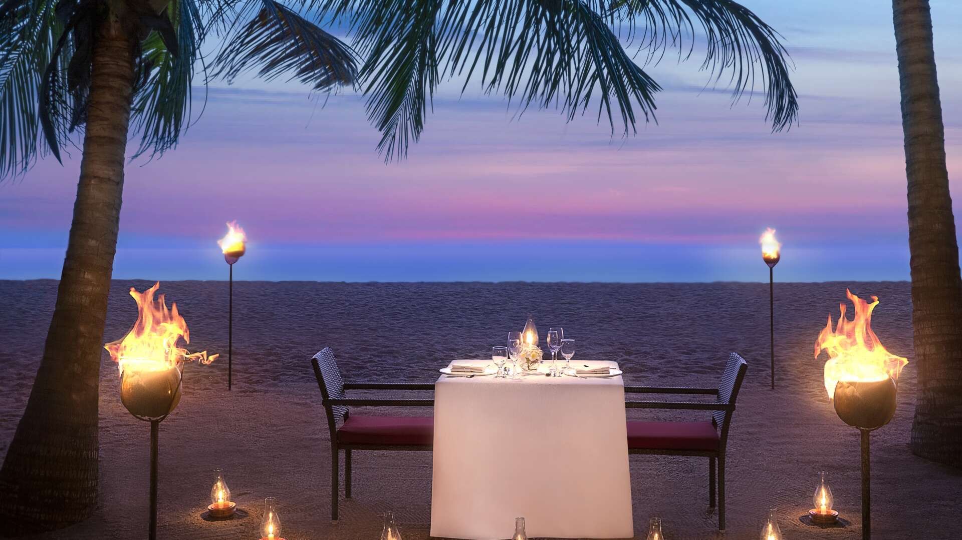 Torch-lit dinner table on the beach at dusk